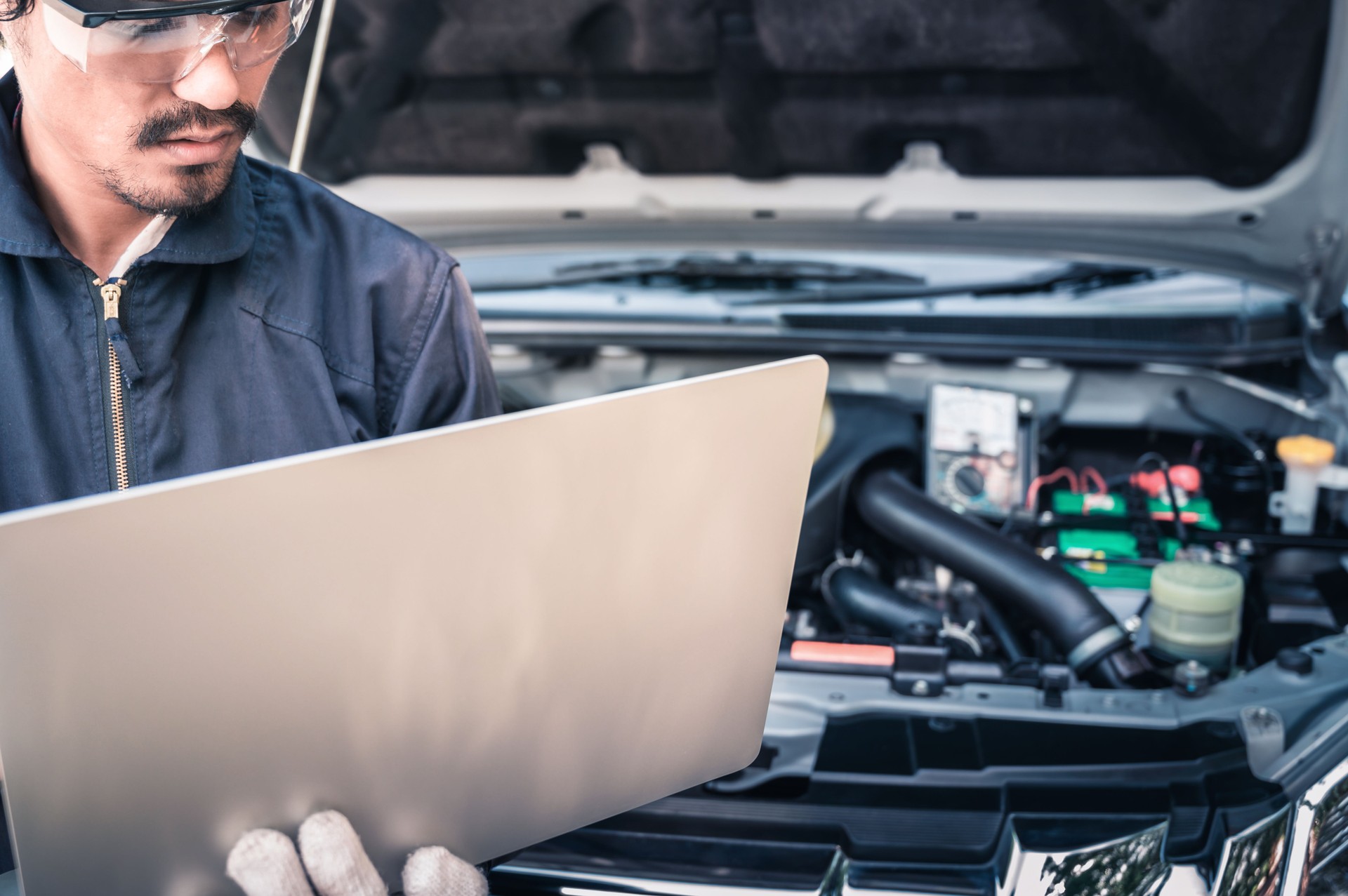 Auto mechanic working on a computer connected to a car engine at repair shop